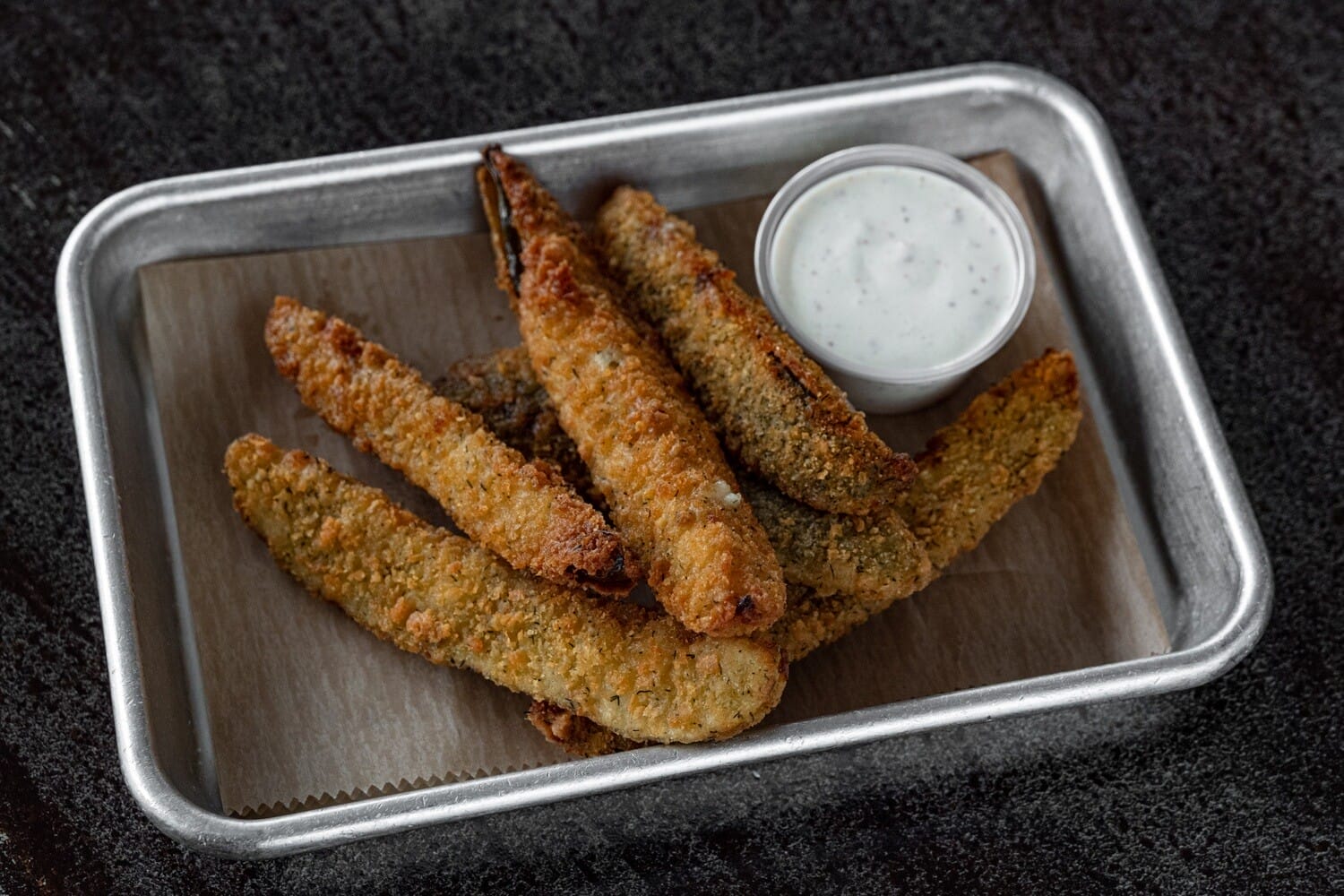 A basket of golden-brown fried dill pickles served with a side of jalapeño ranch dipping sauce at Station 24 Flat Rock.