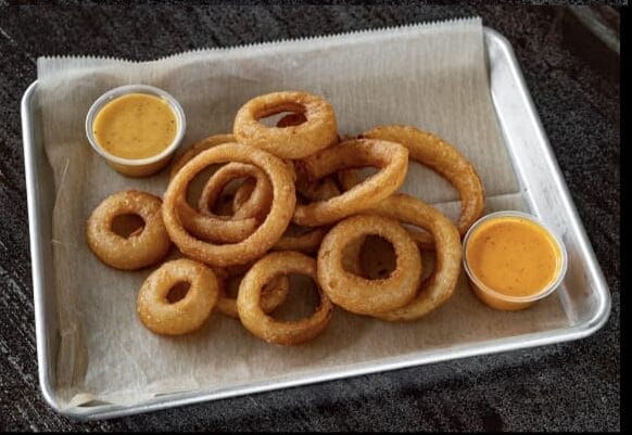 Close-up of crispy golden beer battered onion rings served in a basket with two dipping sauces, Station and Bomb.